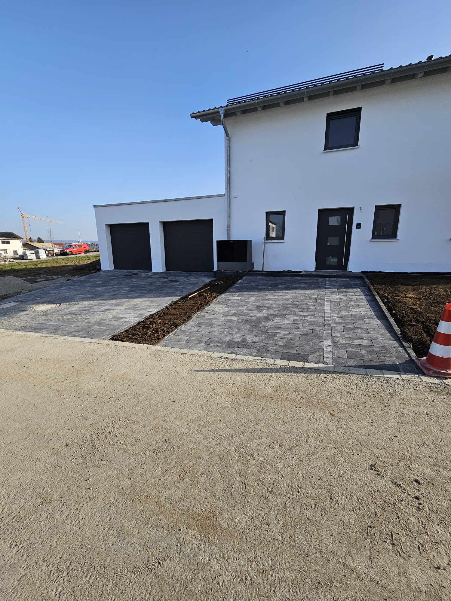 Gepflasterte Einfahrt mit grauen Betonsteinen vor Doppelgarage eines Neubaus