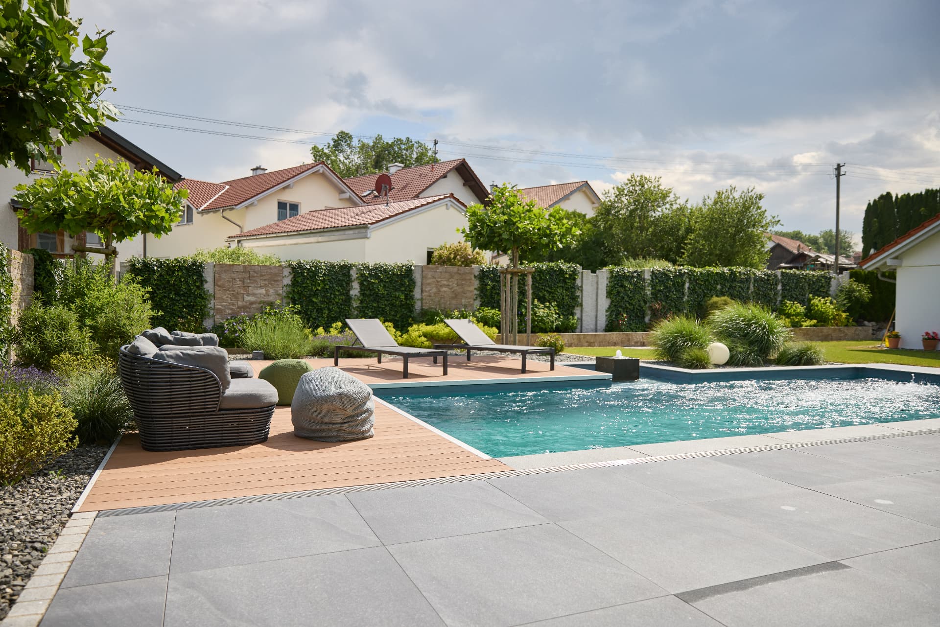 Terrasse mit grauen Platten, Sitzbereich und Bepflanzung in einer Außenanlage in Kempten